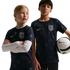 A girl and boy wear navy blue star-patterned USA soccer jerseys; the boy holds a soccer ball. Black background.