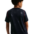 Rear view of a child wearing a navy blue short-sleeved t-shirt with a tonal star pattern and red piping along the shoulders.