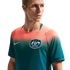 A man wearing an Australian national soccer team jersey with a salmon-to-teal color gradient, featuring the team crest and a white Nike logo. He is looking off-camera against a solid black background.