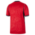 Back view of a red short-sleeve soccer jersey featuring a tonal lion and "ENG" pattern, navy blue side panels with white piping, and navy-striped sleeve cuffs.