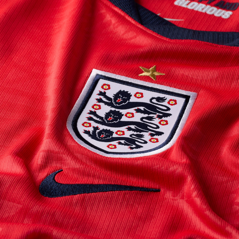 Close-up of a red England football jersey featuring the Three Lions crest with a gold star above it and a dark blue Nike swoosh below.