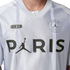 Close-up of a white PSG jersey featuring a large black 'PARIS' graphic with a Jumpman logo replacing the letter 'A', faint grey stripes, and team crest.