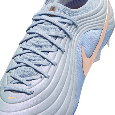 Close-up of a light blue Nike soccer cleat featuring a textured wavy upper, a rose gold Swoosh, and light blue laces against a black background.