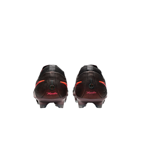Rear view of dark soccer cleats with "Maestro" in pink script and orange accents on the heels, set against a black background.