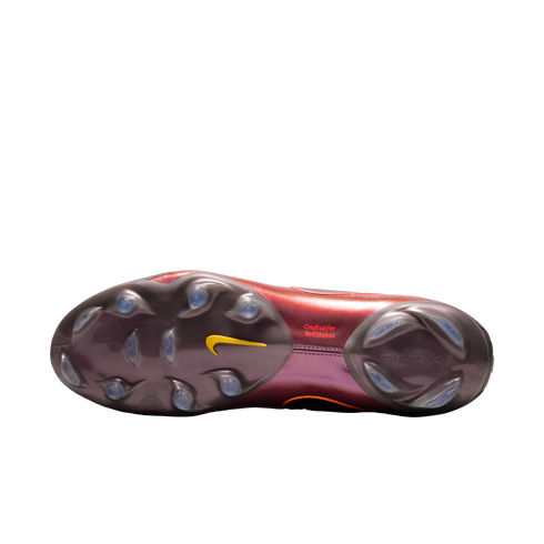 Bottom view of an iridescent maroon Nike soccer cleat soleplate with clear studs, a yellow swoosh, and "Crafted for Brilliance" text, set against a solid black background.
