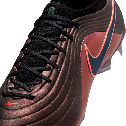 Close-up of a textured bronze Nike soccer cleat with black laces and an iridescent blue swoosh outlined in pink.