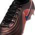 Close-up of a textured bronze Nike soccer cleat with black laces and an iridescent blue swoosh outlined in pink.