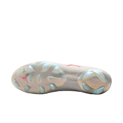 The sole of a Nike x Jordan soccer cleat featuring iridescent plates, molded studs, a red Jumpman logo, and a white swoosh against a gray patterned upper.