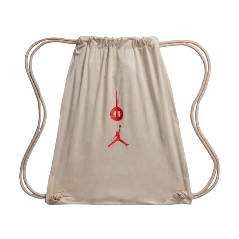 Beige suede drawstring backpack with thin rope straps. Features red embroidered Jordan Brand Jumpman and circular logos on the front center.