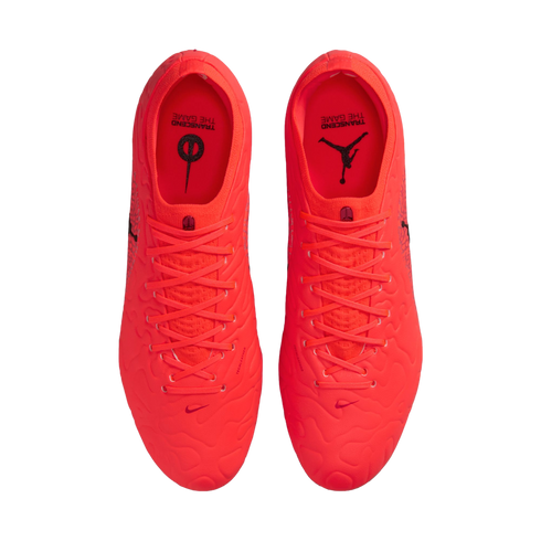 Top-down view of vibrant neon orange Nike and Jordan soccer cleats on a black background, with "TRANSCEND THE GAME" text on the insoles.