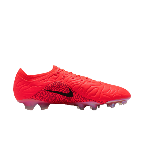 Profile view of a bright red Nike soccer cleat with a textured wavy upper and a black swoosh over a patterned midfoot panel, set against a black background.