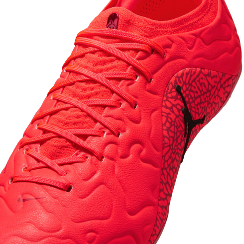 Close-up of a bright red soccer cleat with matching laces, a textured upper, and a black Jumpman logo on the side against a black background.