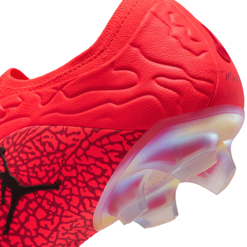 Close-up of a red Jordan soccer cleat heel featuring textured patterns, a black Jumpman logo, and a translucent, iridescent soleplate.