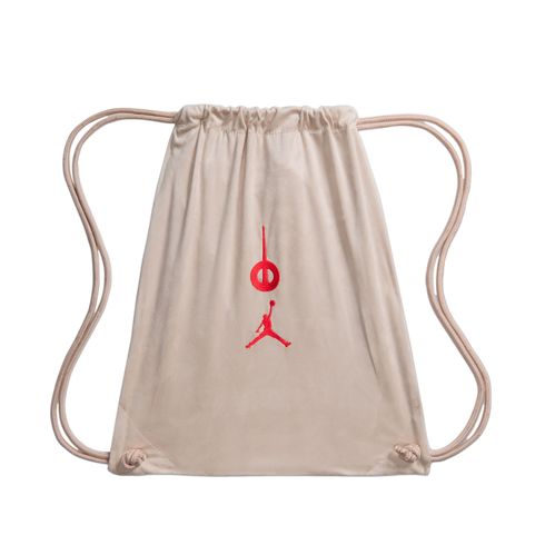 A light tan suede drawstring bag with a red embroidered Jordan Jumpman and a circular logo on the front, isolated on a black background.