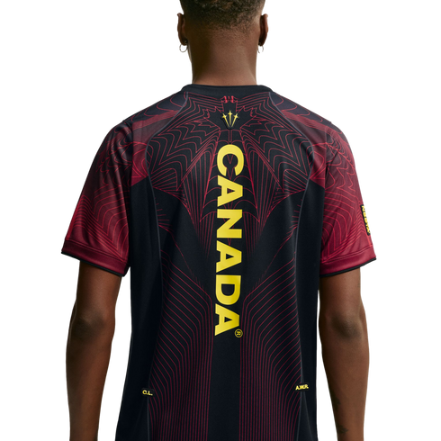 Back view of a person wearing a black jersey with "CANADA" in vertical yellow text down the center, featuring intricate red line patterns on the shoulders and back.