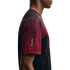 Side profile of a person wearing a maroon and black jersey with graphic line patterns and a yellow "NOCTA" label on the sleeve.