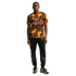 A man poses in a patterned orange and black jersey, black joggers featuring silver lion graphics, and silver Nike sneakers, all against a white background.