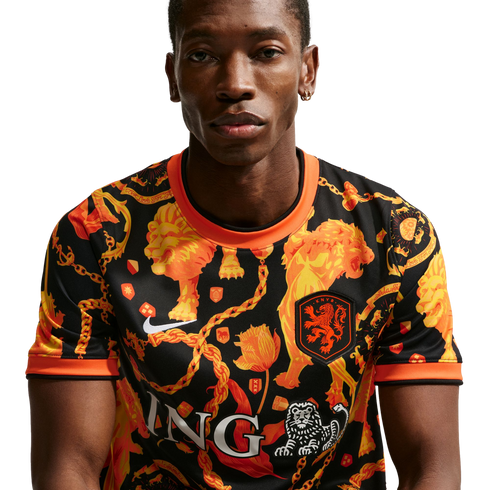 A man models a black Nike Netherlands national soccer jersey with a vibrant orange pattern of lions and chains. Plain white background.
