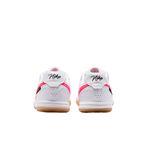 Rear view of a pair of white Nike sneakers with pink accents, gum rubber soles, and script "Nike" branding on the heels.