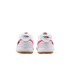 Rear view of a pair of white Nike sneakers with pink accents, gum rubber soles, and script "Nike" branding on the heels.