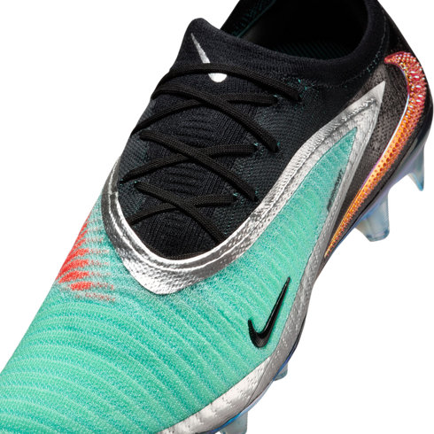 Close-up of a Nike soccer cleat with a teal textured upper, black lace area, metallic silver trim, and a large iridescent orange swoosh on the heel.