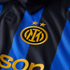 Close-up of an Inter Milan soccer jersey featuring black and blue sawtooth stripes, a gold embroidered club crest, and two gold stars above it.