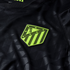Close-up of a black soccer jersey with a lime green Atlético Madrid crest. The fabric features a subtle tonal geometric pattern.