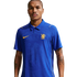 A man wearing a blue, collared Chelsea FC jersey with yellow logos and a large textured crest on the chest, isolated on a white background.