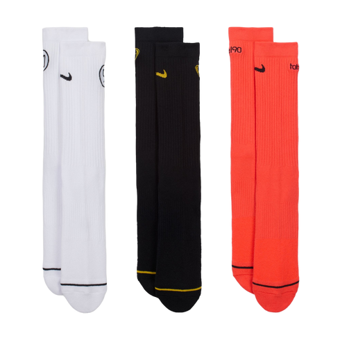 Three pairs of Nike Total 90 crew socks in white, black, and bright orange, displayed vertically against a black background. Each features a small swoosh and a contrasting line near the toe.