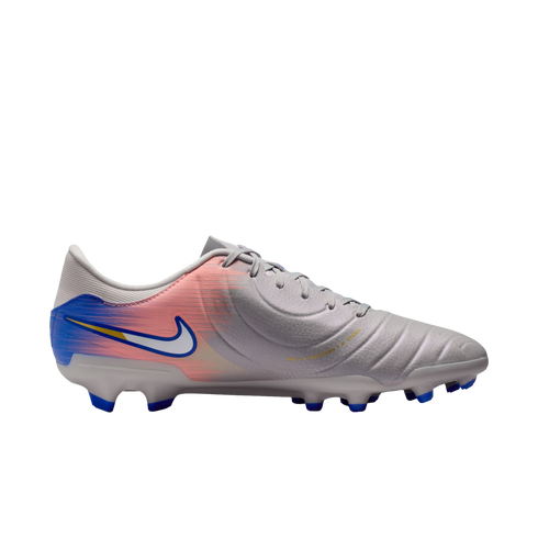 Side view of a light gray Nike soccer cleat with a pink and blue gradient design on the heel and blue studs, set against a black background.