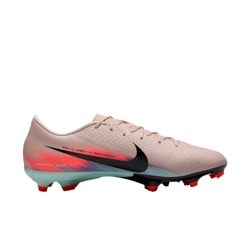 Side view of a light pink Nike soccer cleat with a black swoosh, red and blue heel graphics, and ".002 x L. JAMES + S. PARALLUELO" text.