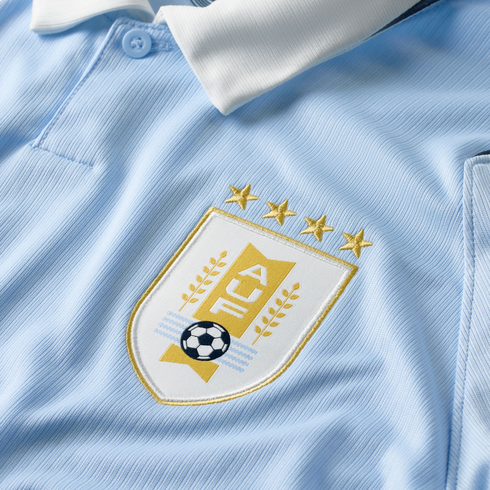 Close-up of a light blue Uruguay soccer jersey with a white collar and an embroidered AUF crest topped by four gold stars.