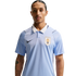 A man with a mustache wears a light blue Uruguay national football team polo shirt with a white collar and Nike logo against a black background.