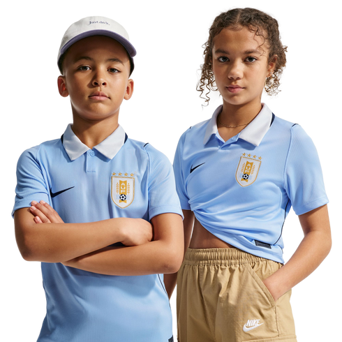 A boy and girl pose in light blue Uruguay national soccer team jerseys and Nike apparel against a black background.