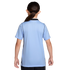 Back view of a person with dark hair in a ponytail wearing a light blue short-sleeved athletic shirt with black trim against a black background.