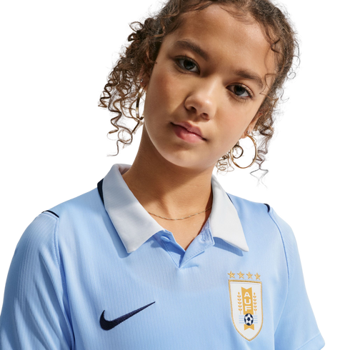 Close-up of a young person with curly hair wearing a light blue Nike Uruguay soccer jersey with a white collar and AUF crest.
