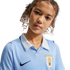 Close-up of a young person with curly hair wearing a light blue Nike Uruguay soccer jersey with a white collar and AUF crest.