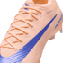 Close-up of a peach-colored Nike soccer cleat with a blue swoosh and a textured knit upper.