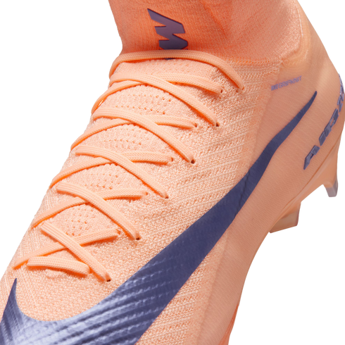 Close-up of a peach-colored Nike soccer cleat featuring a textured knit upper, matching laces, and a large purple swoosh.
