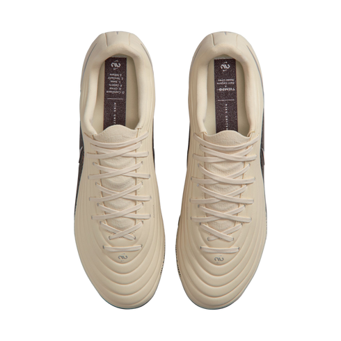 Top-down view of a pair of cream-colored Nike Tiempo soccer cleats with matching laces, displayed against a solid black background.