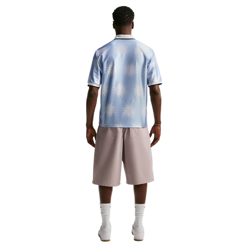 Back view of a man wearing a light blue sunburst-patterned polo shirt, mauve shorts, white socks, and white sneakers.