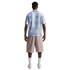 Back view of a man wearing a light blue sunburst-patterned polo shirt, mauve shorts, white socks, and white sneakers.