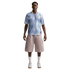A man wearing a light blue sun-patterned soccer jersey, tan shorts, and white sneakers stands against a plain white background.