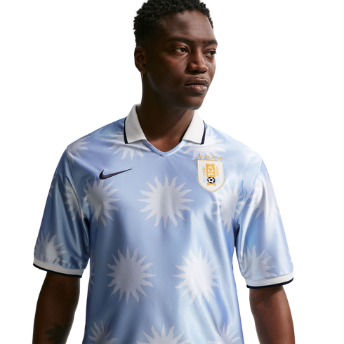 A man in a light blue Nike Uruguay football jersey with a white sun pattern and polo collar, looking to the side against a white background.