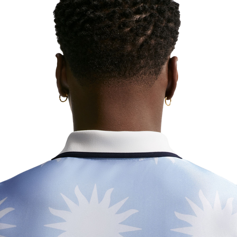 Back view of a person with short curly hair and gold hoop earrings, wearing a light blue polo shirt with a white sun pattern.