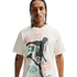 A young man with braided hair and a thin mustache wearing a cream-colored T-shirt with a large soccer-themed graphic, set against a solid black background.