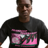A person wearing a black Nike t-shirt with a pink and green "FRIENDSHIP TOURNAMENT" soccer graphic on the front.
