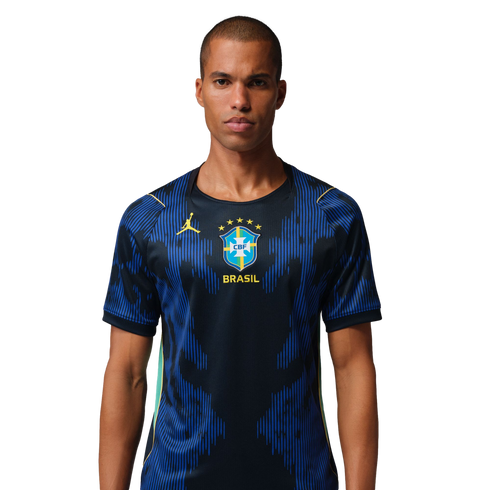 A man in a dark blue Brazil football jersey with a yellow Jordan logo and CBF crest, featuring blue vertical patterns, against a black background.
