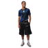 A male model wears a blue Brazil national team soccer jersey, black shiny shorts, and Jordan sneakers, standing against a black background.