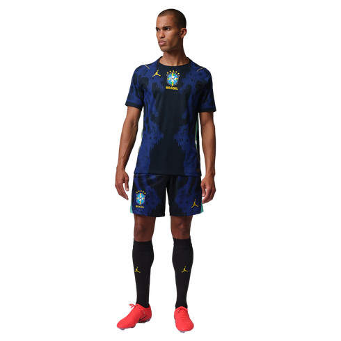 A man wearing a blue and black Brazil soccer kit with yellow Jordan logos and red cleats against a black background.